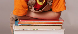 Bücherstapel, darauf noch zu sehen, die verschränkten Arme eines Kindes, das sich darauf abstützt